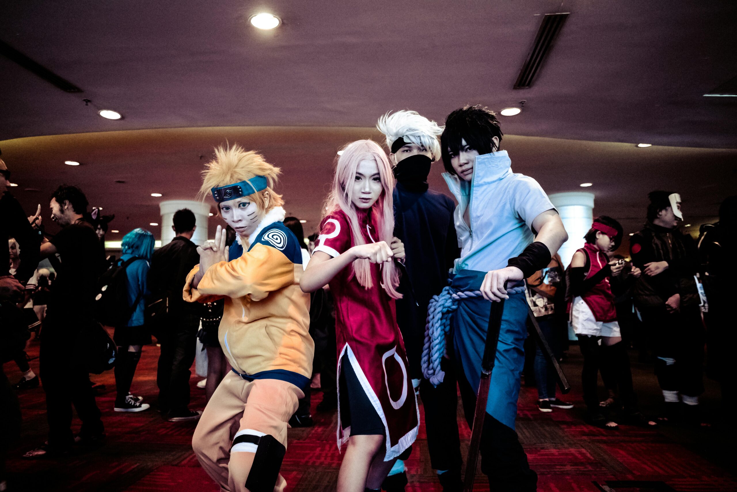 A lively group of cosplayers in anime costumes posing at an indoor convention event.