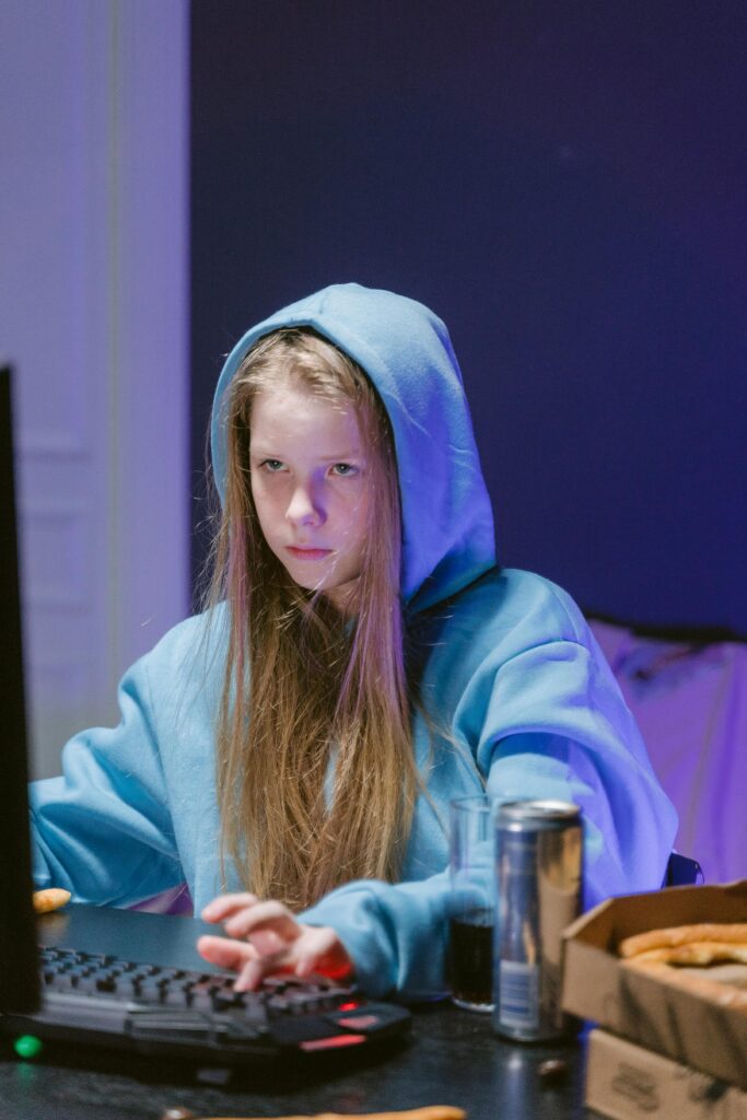 Teen girl focused on computer game wearing hoodie indoors, symbolizing modern gaming leisure.