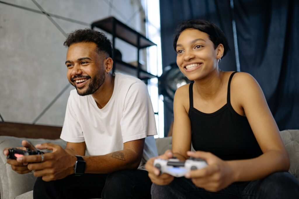 A couple playing video games on a sofa, engaged and smiling indoors.